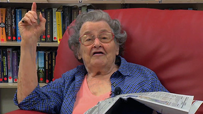 Elderly woman talking while seating on a couch and holding a news paper